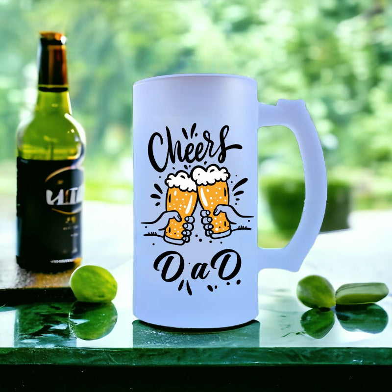 White mug with 'Cheers DAD' text and beer graphics next to a bottle on a green surface.