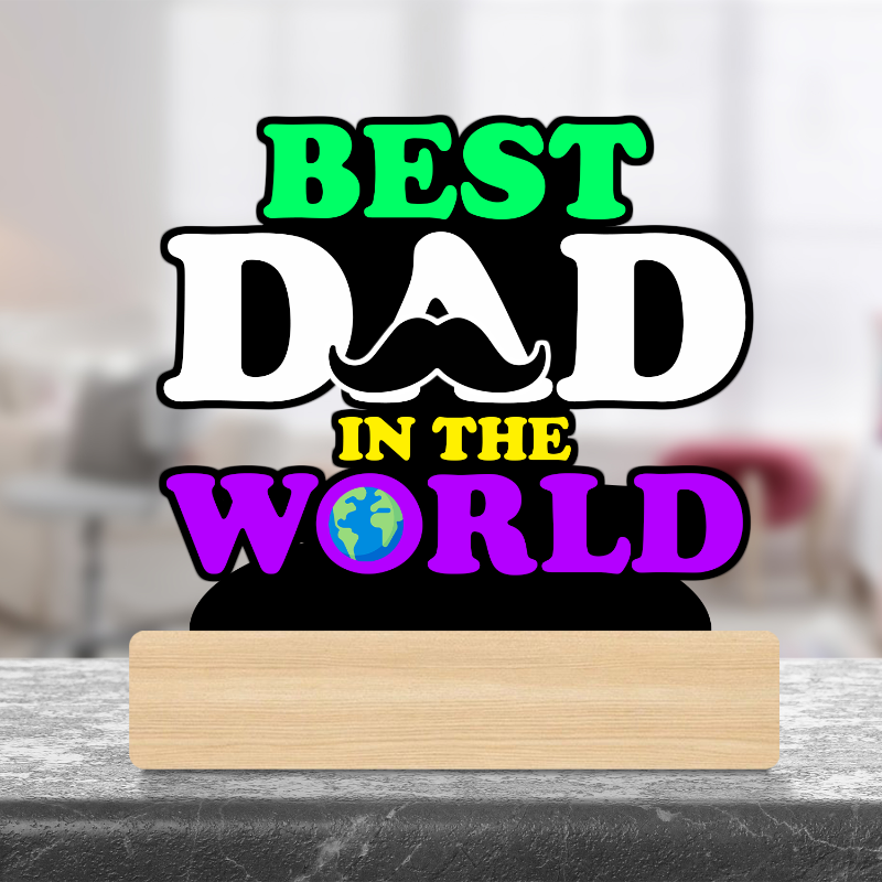 A wooden desk decor sign that reads 'BEST DAD IN THE WORLD' in bold letters, placed on a desk against a blurred background.