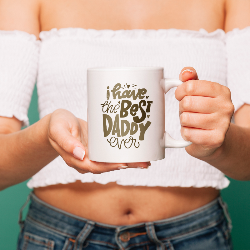 Person holding a mug with 'I have the best daddy ever' text against a teal background