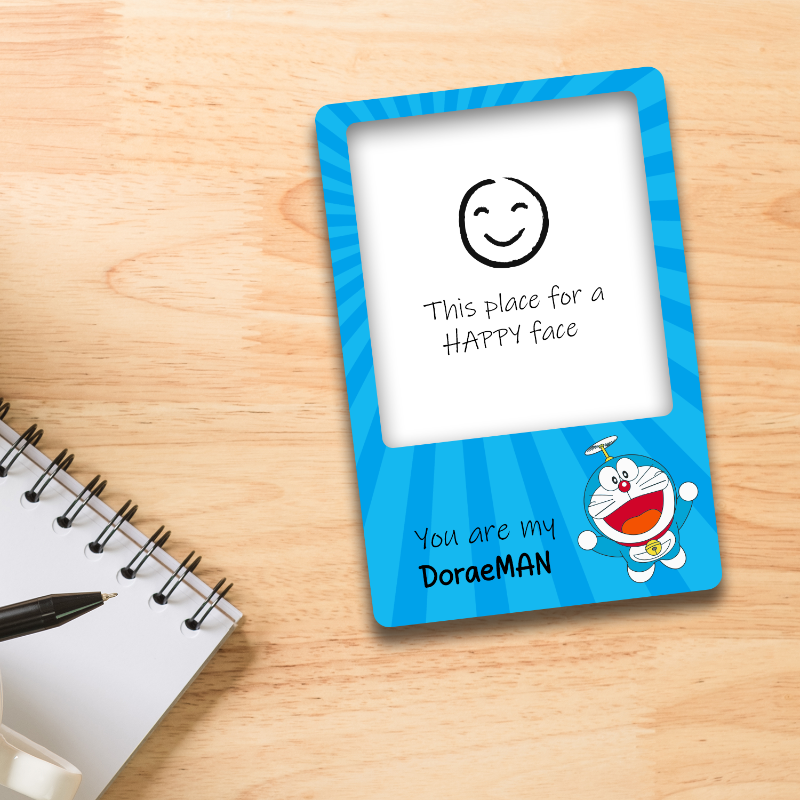 Card with Doraemon design on a wooden surface next to a notebook and pen