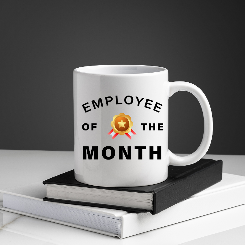 White mug with 'Employee of the Month' text on a stack of books against a dark background