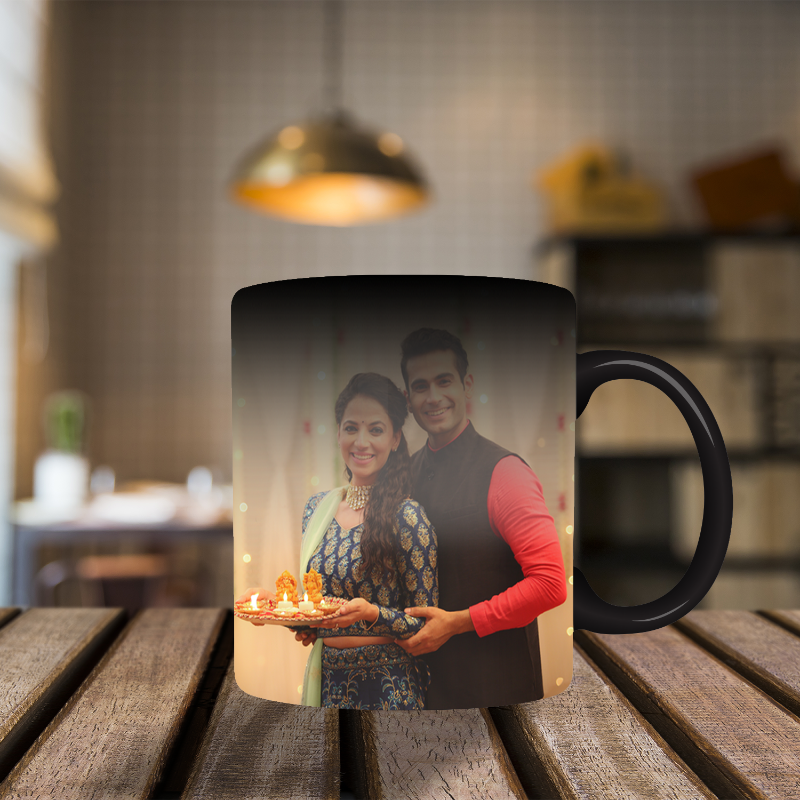Black mug with a printed design of a couple holding a tray with candles on a wooden surface.