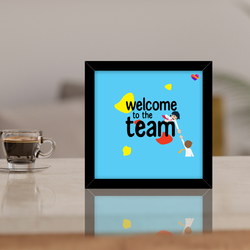 Framed artwork with 'welcome to the team' text on a table with a cup of coffee.