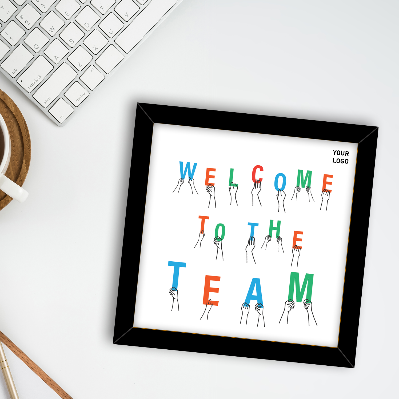 Framed print with 'Welcome to the Team' text on a desk with a keyboard and mug.