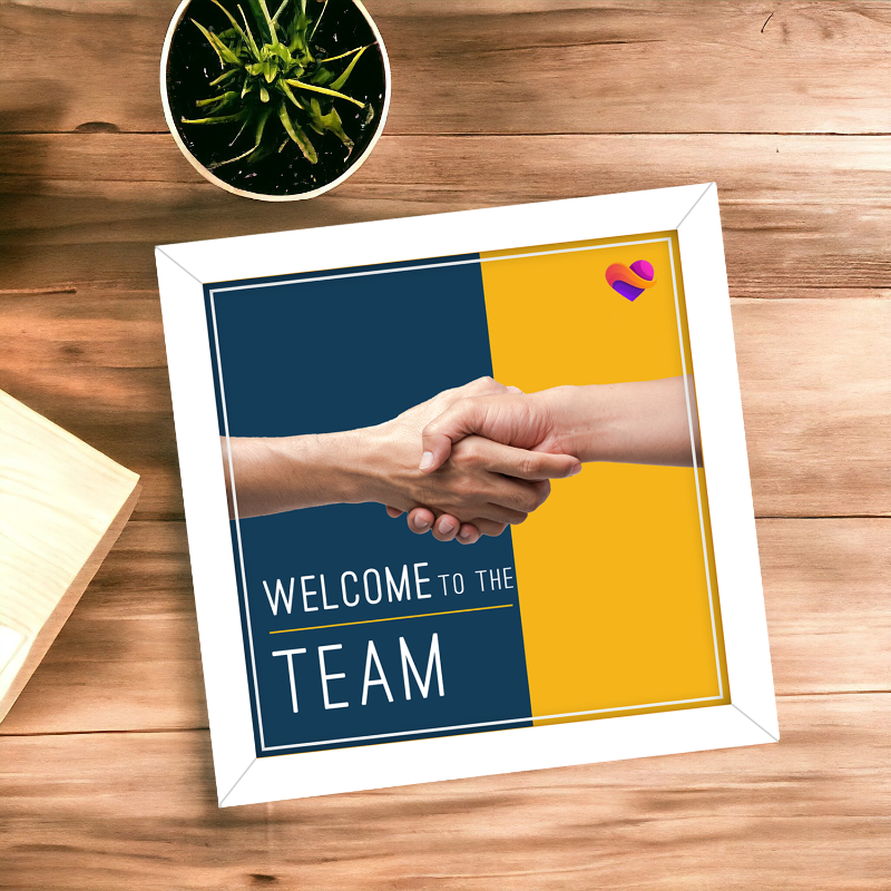 Framed poster with handshake illustration and 'Welcome to the Team' text on a wooden surface.