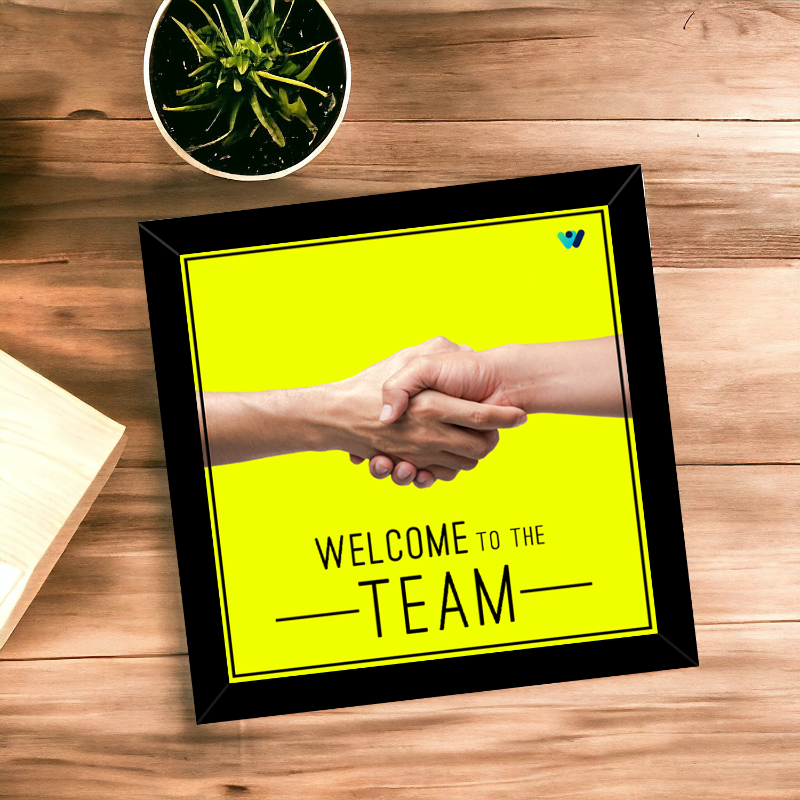 Framed picture of two hands shaking with 'Welcome to the Team' text on a wooden surface.