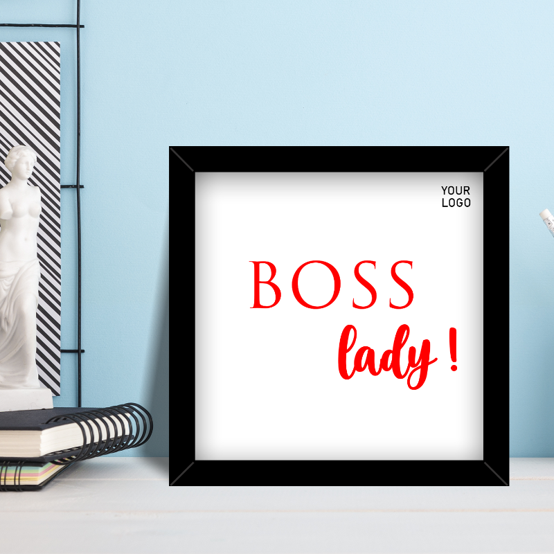 A rectangular frame with a white background, featuring the text 'BOSS LADY!' in red and black, presented on a desk with office supplies around.