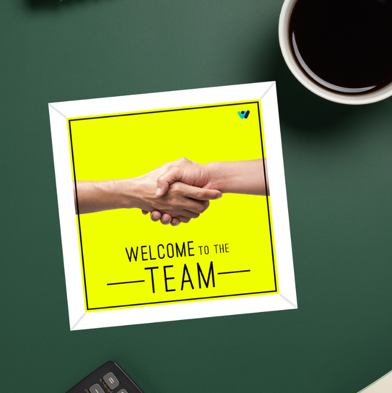 Framed picture of two hands shaking with 'Welcome to the Team' text on a green surface with a cup of coffee.