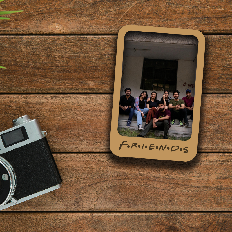 Wooden photo frame with a group photo on a wooden surface next to a vintage camera.
