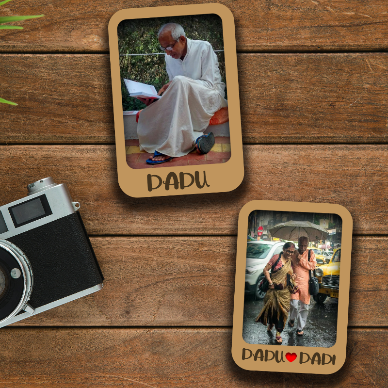 The image shows a set of two personalized wooden fridge magnets. One magnet has a photo of an elderly man sitting, and the other has a photo of an elderly woman standing, both with the text 'Dadu' and 'Dadi' respectively.