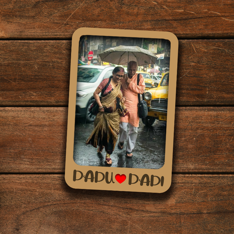 Card with a photo of two people walking under an umbrella on a wooden surface, featuring 'DADU' and 'DADI' text.