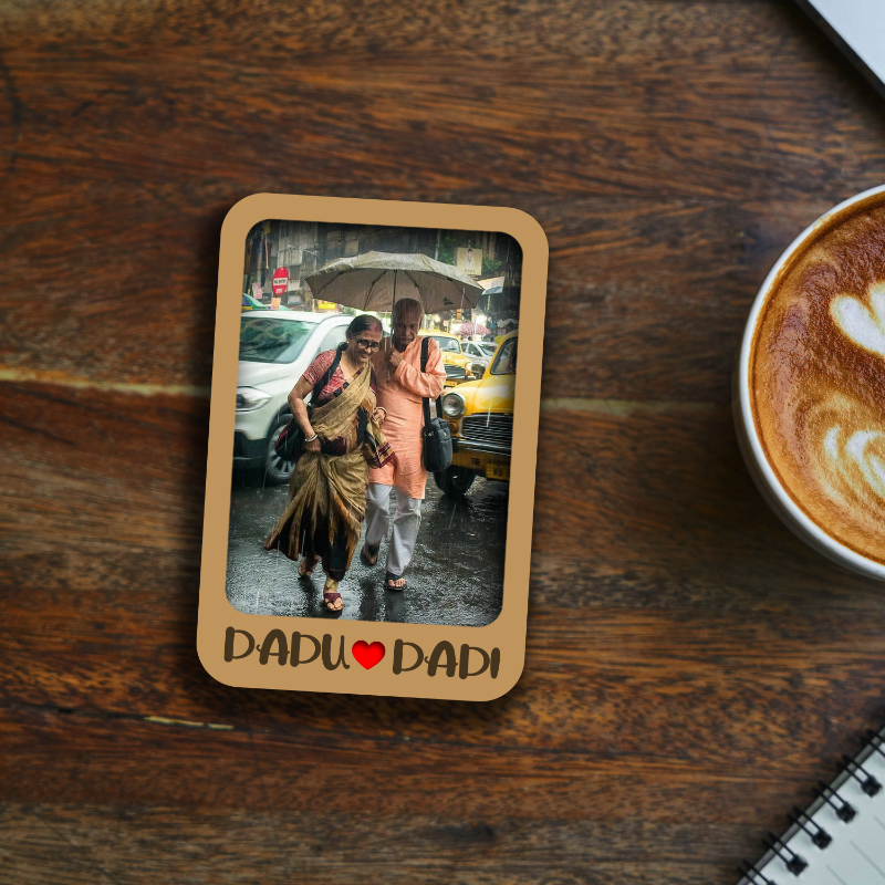 Framed photo of two people with an umbrella on a wooden table next to a cup of coffee.