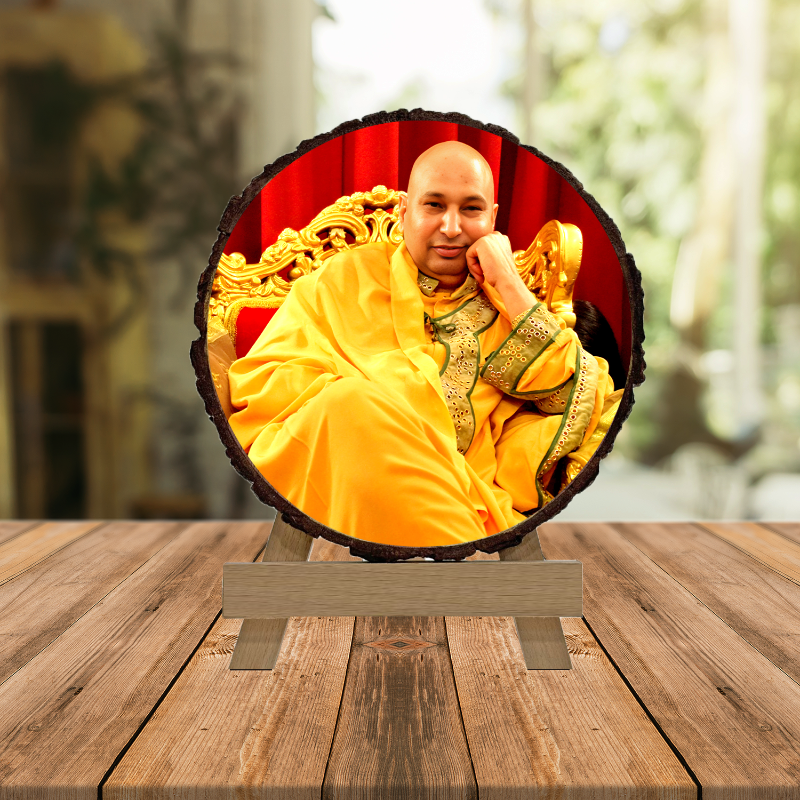 A photo of a man in a yellow robe seated on a throne-like chair, placed within a round wooden frame that is set on a wooden surface.