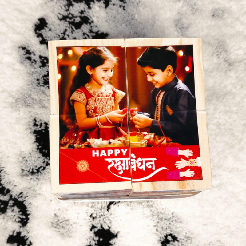 A wooden photo cube with a happy Raksha Bandhan message, featuring images of a brother and sister on the front panels, placed on a snowy surface.