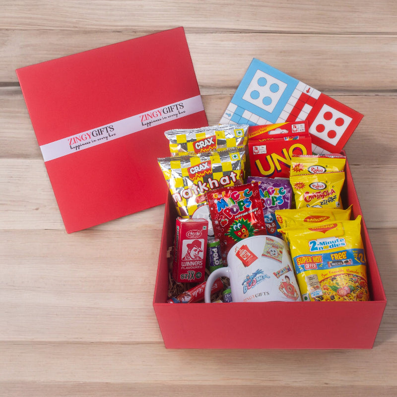Red gift box with snacks and a mug on a wooden surface, featuring Zingy Gifts branding.