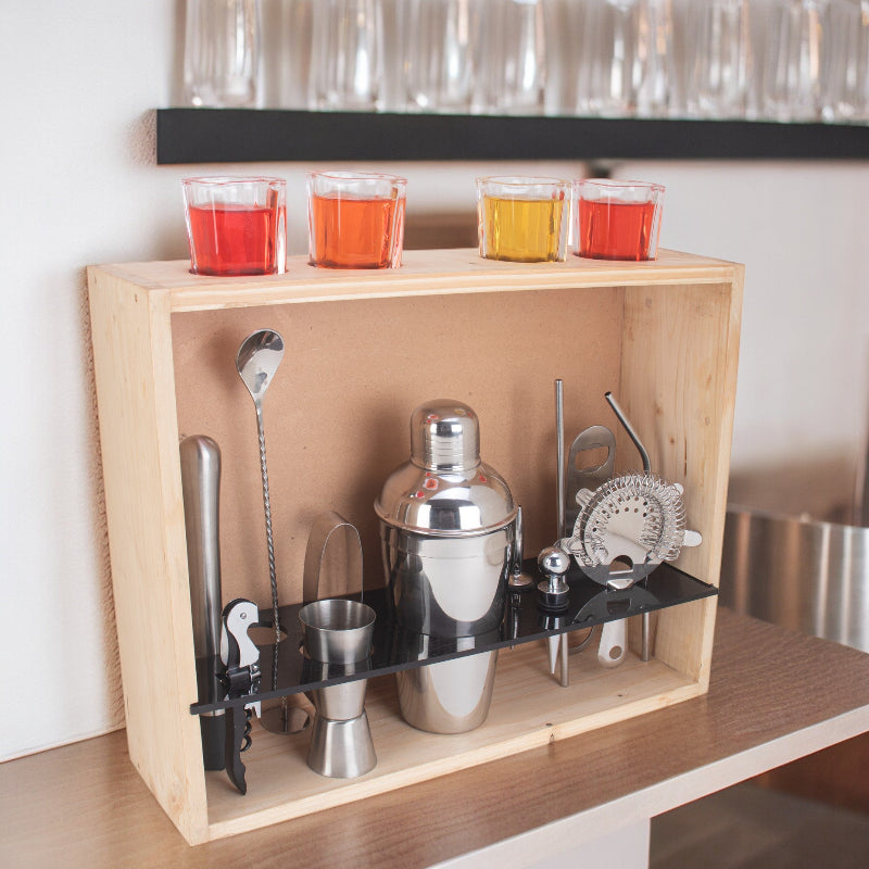A 17-piece barware set with a military grey wall stand, including tools such as a cocktail shaker, jigger, mixing spoon, strainers, pourers, tongs, bottle opener, corkscrew, zester/peeler, wine stopper, straw, and four shot glasses, displayed on a wooden shelf.