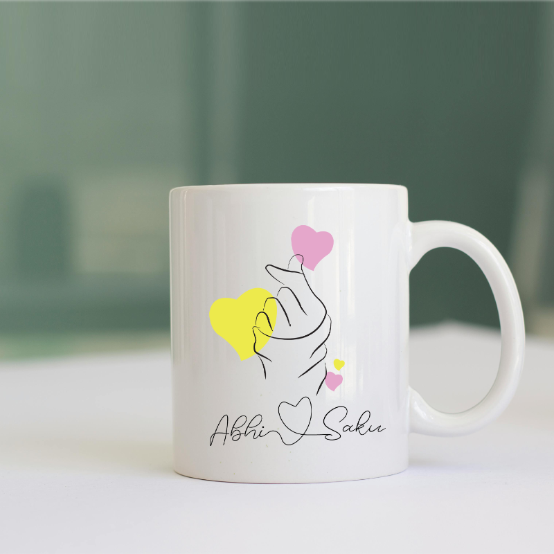 White mug with artistic design and names 'Abhi' and 'Sakshi' on a blurred background