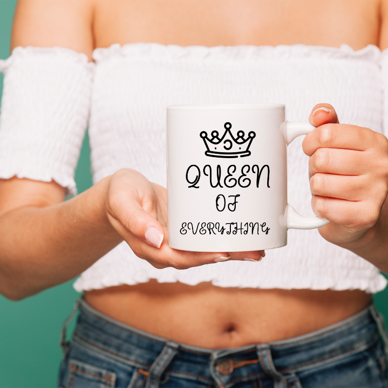 Person holding a white mug with 'Queen of Everything' text and crown design.