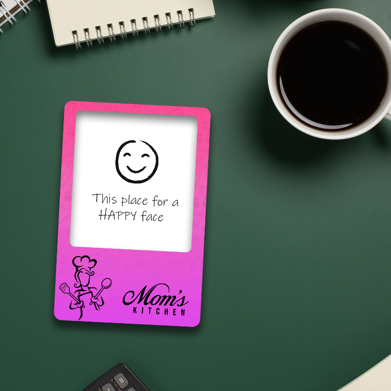 Pink electronic device with a smiley face and text on a green surface with a cup of coffee.