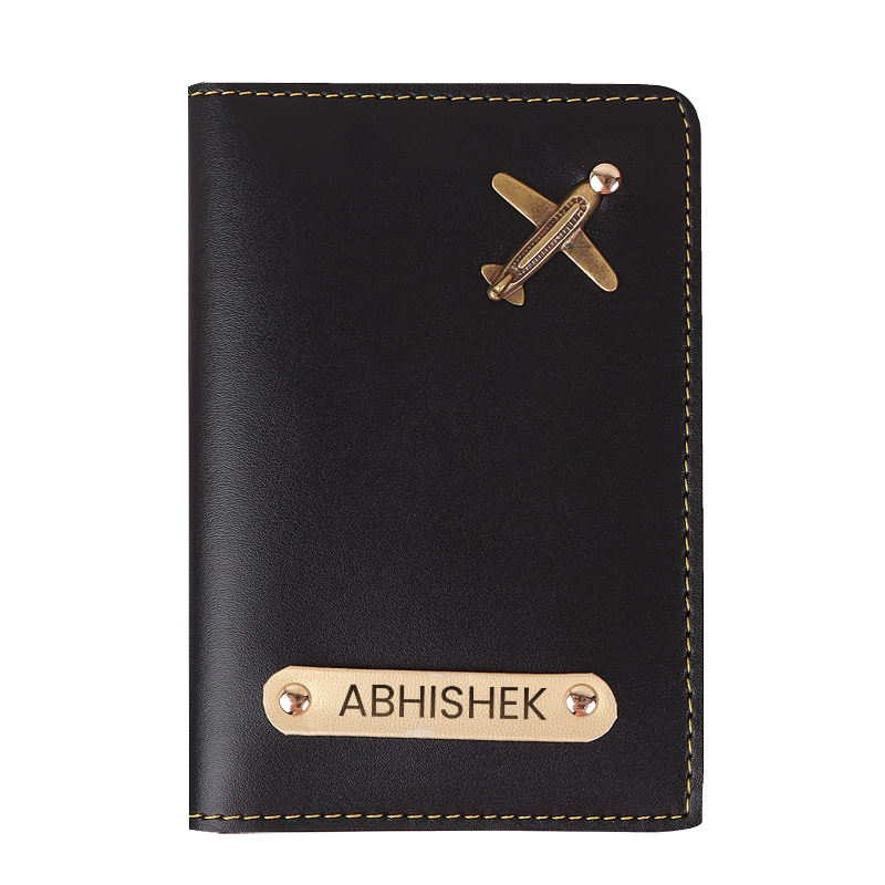 Black passport holder with gold airplane and name tag on a white background