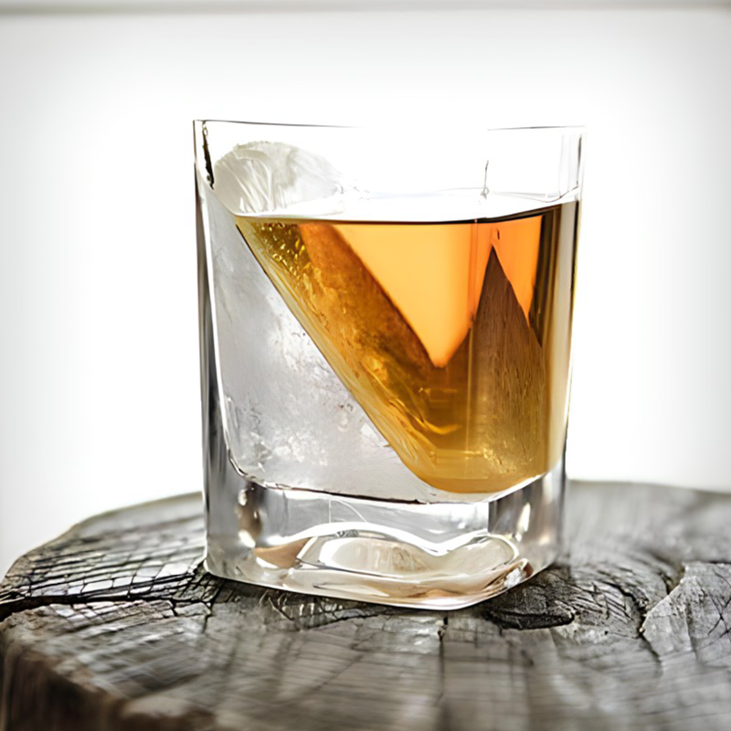Clear glass with amber liquid and ice on a wooden surface
