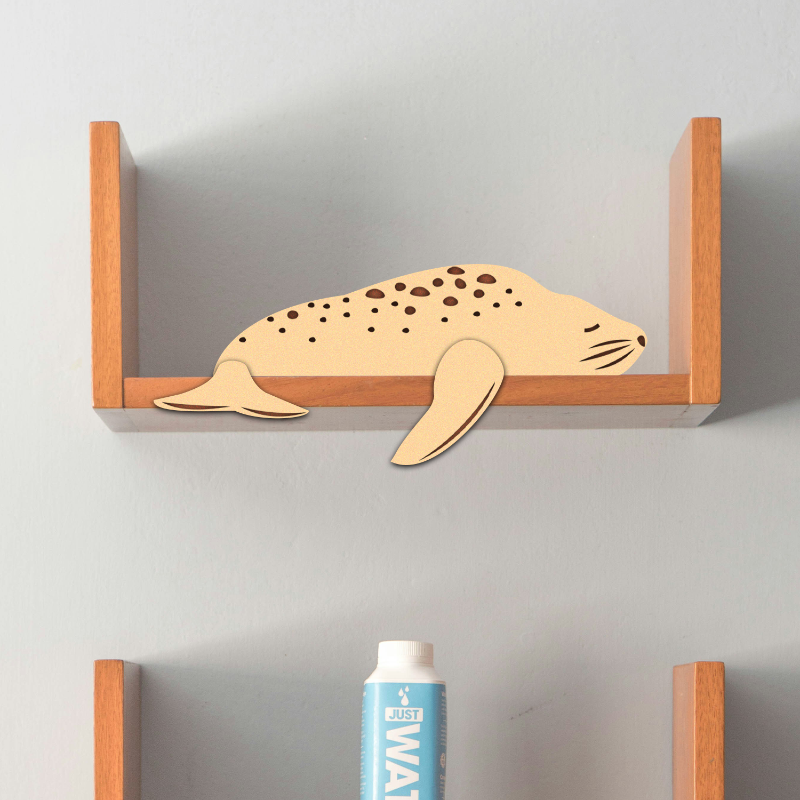 Wooden figurine of a lazy seal placed on a shelf, with a blue and white bottle in front.
