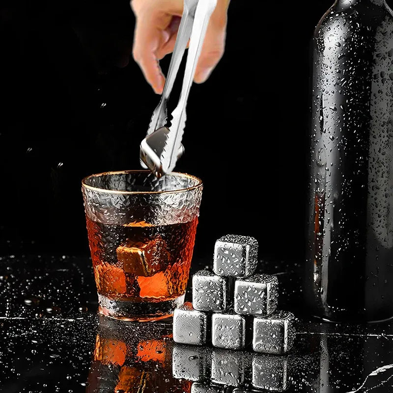 Stainless steel ice cubes being added to a glass of liquid with a dark background