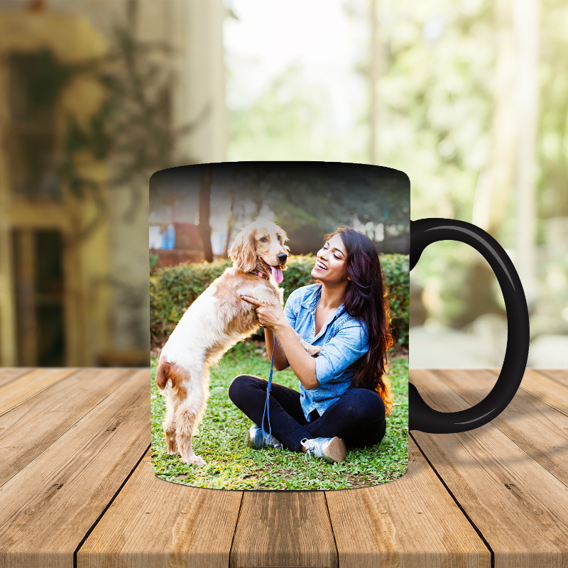 Black mug with a photo of a woman and dog on a wooden table outdoors