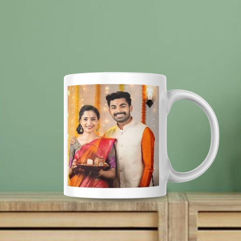 A ceramic mug with a personalized photo of a couple celebrating Karva Chauth. The man is holding a plate with sweets, and the couple is smiling and posing for the camera.