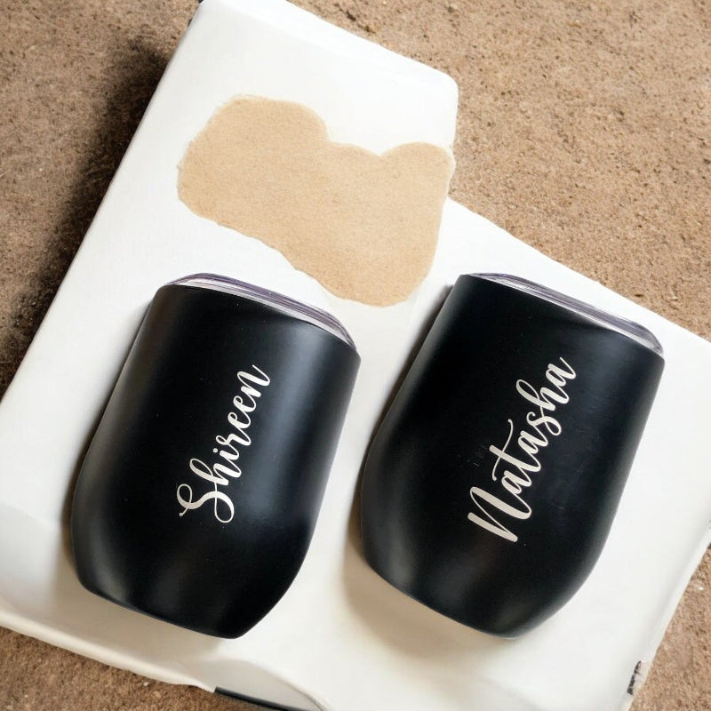 Two black tumblers with names engraved on them, placed in a white box.