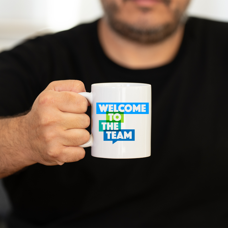 Person holding a white mug with 'Welcome to the Team' text in colorful letters.