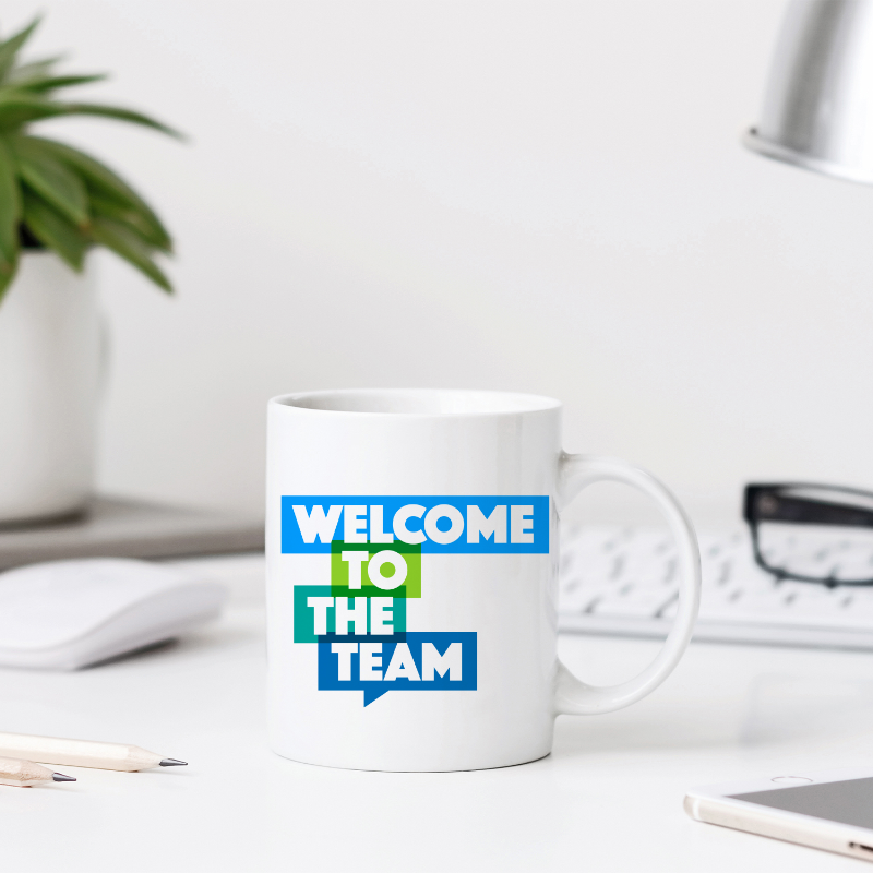 White mug with 'Welcome to the Team' text on a desk with office items.