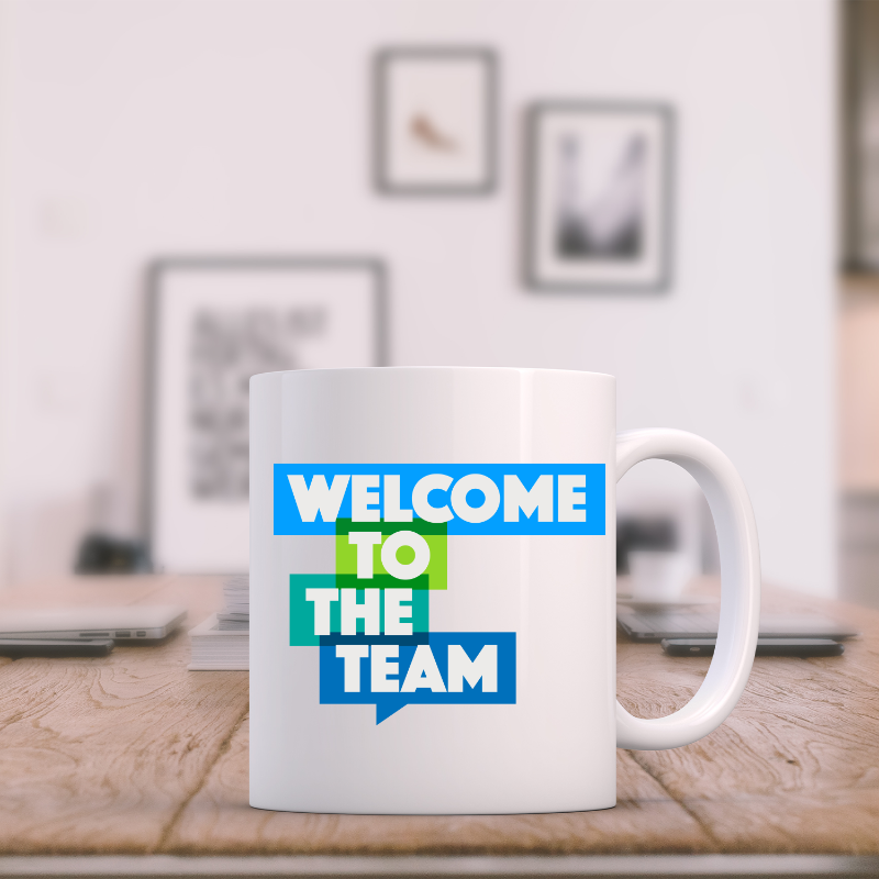 White mug with 'Welcome to the Team' text on a desk with blurred office background