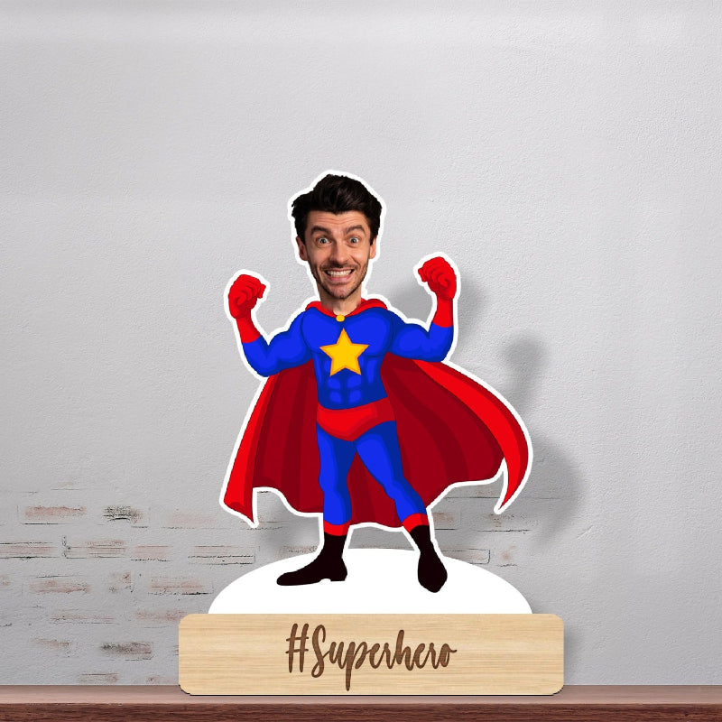 A personalized superhero caricature standing on a wooden stand with a hashtag '#Superhero' at the bottom. The caricature is depicted in a colorful superhero costume, posed with one hand raised and a smile on its face.