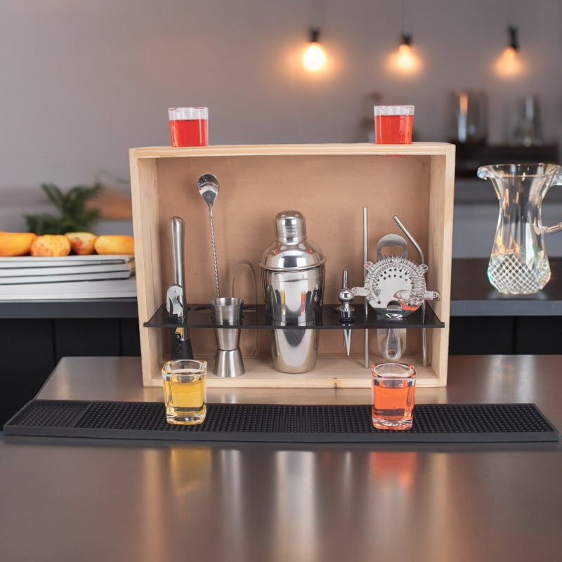Bar set with cocktail shaker, jigger, and strainer on a wooden tray with drinks in the background.