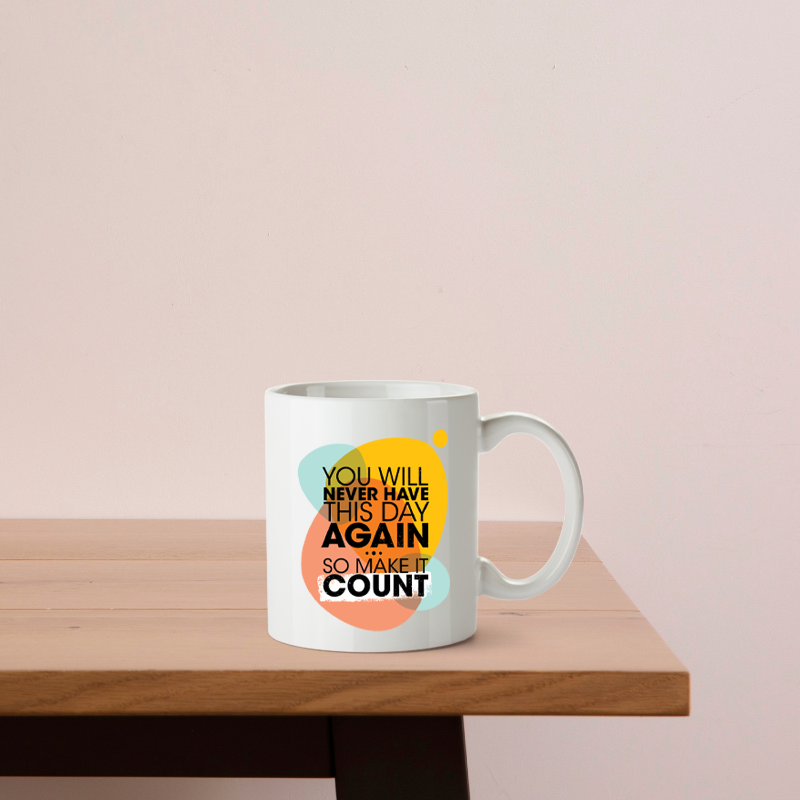 White mug with colorful text on a wooden table against a light pink background