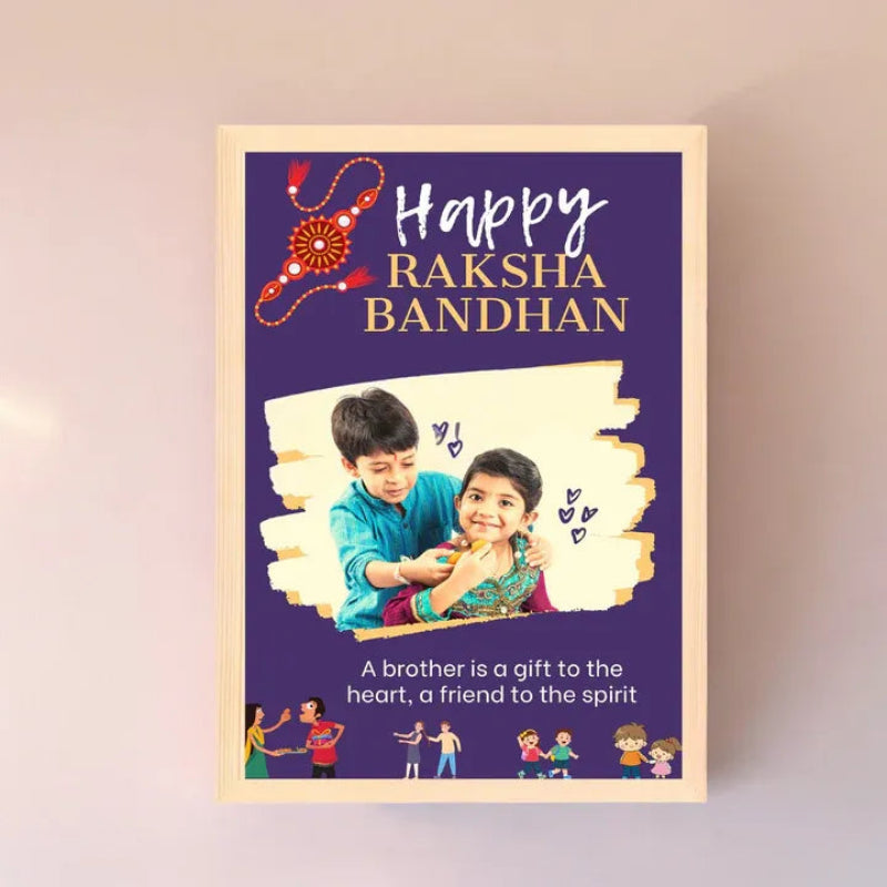 A framed personalized Raksha Bandhan greeting card or poster displayed against a light beige wall. The card has a deep purple background with 'Happy Raksha Bandhan' in white and gold text, a red and gold decorative thread illustration, a photo of a brother and sister, and additional text and small cartoon figures at the bottom.