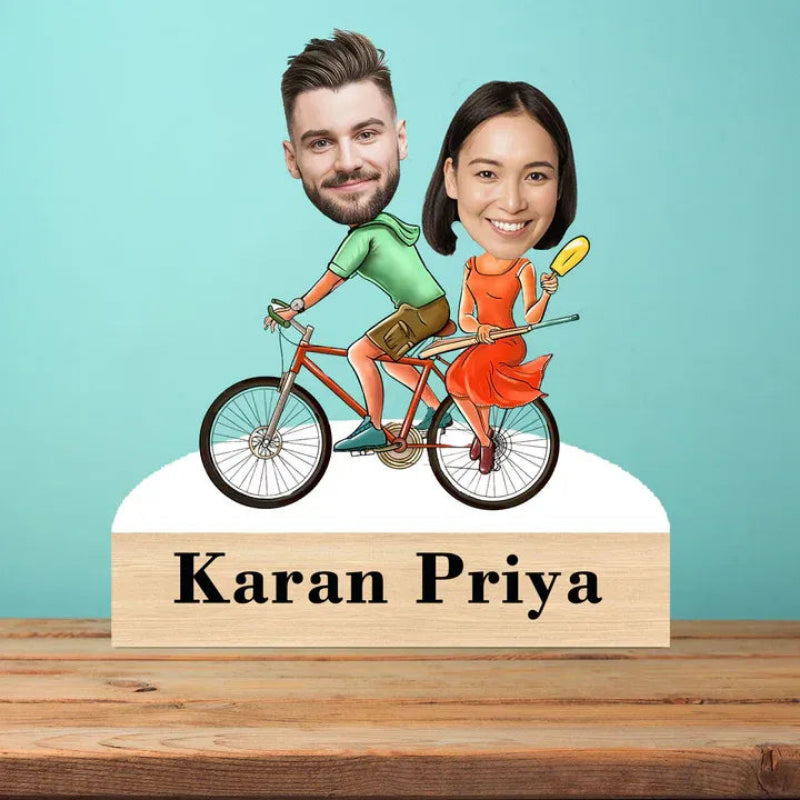 Caricature of a man and woman on a bicycle with 'Karan Priya' below, against a teal background.