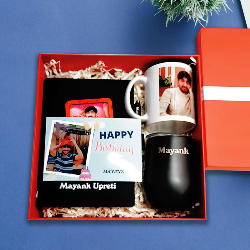 Gift set with mug, black tumbler, and photo album in an open red box on a blue background.