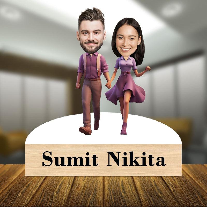 Bobblehead figures of a man and woman holding hands with a wooden base displaying 'Sumit Nikita' on a blurred indoor background.