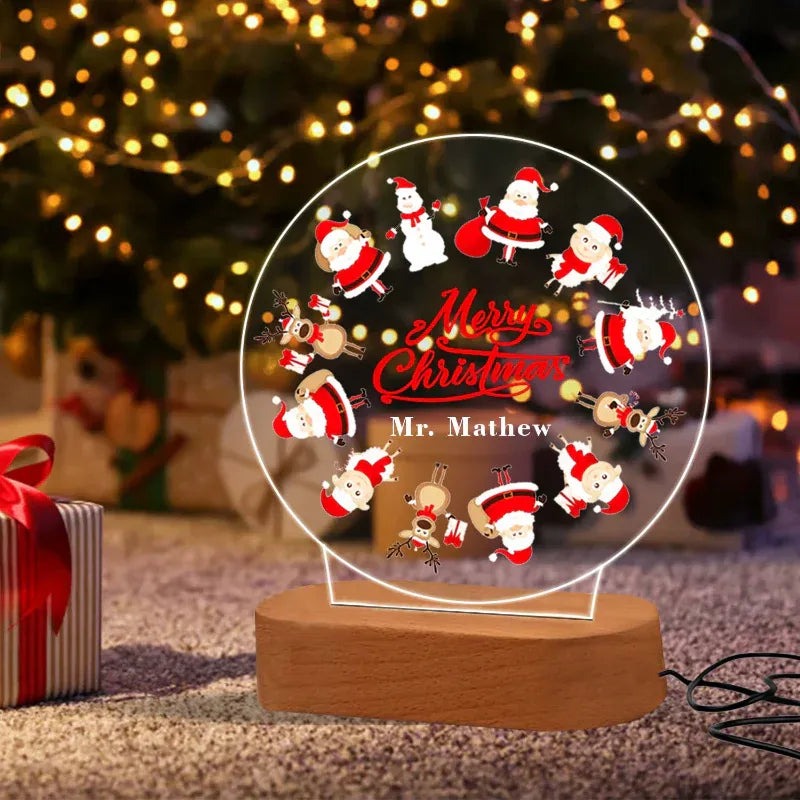 Christmas-themed decorative light with Santa Claus and reindeer design, placed in front of a decorated Christmas tree.