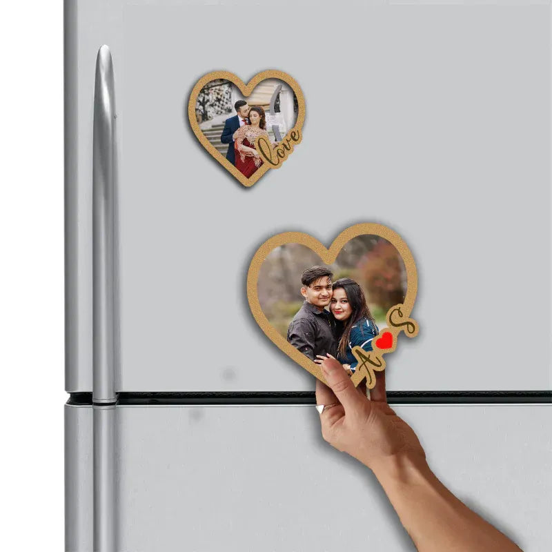 Couple Heart-shaped photo magnets on a refrigerator with a hand placing one on the door.