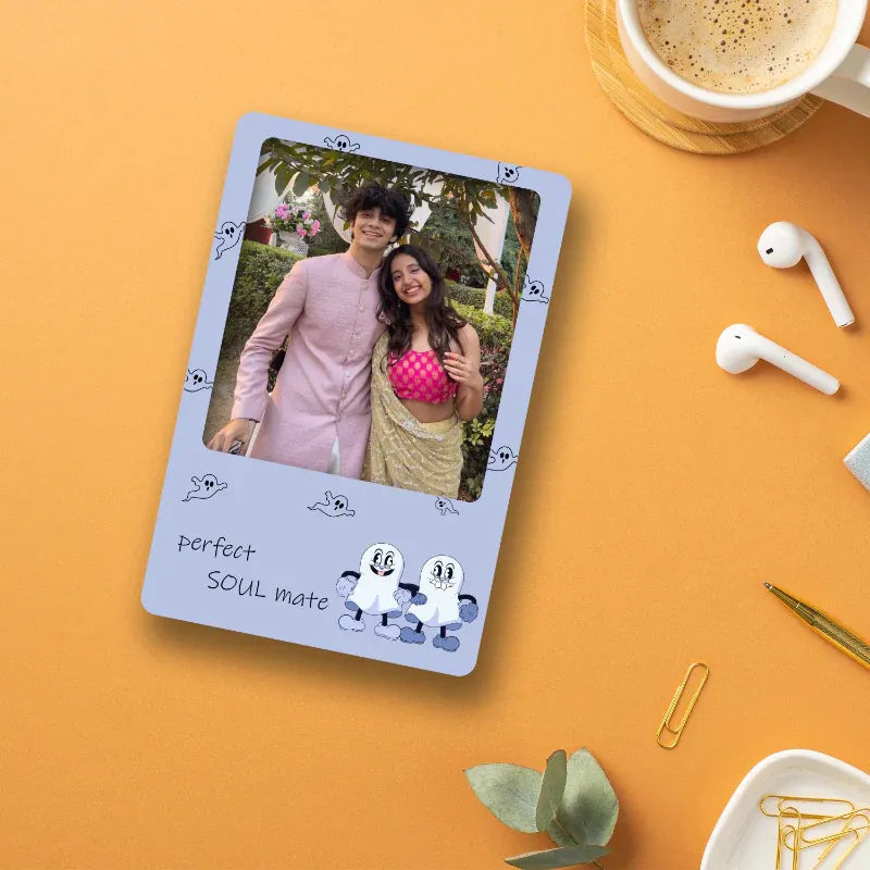 Playing card with a photo of a couple labeled 'Perfect SOUL mate' on an orange surface with a cup of coffee and earbuds.