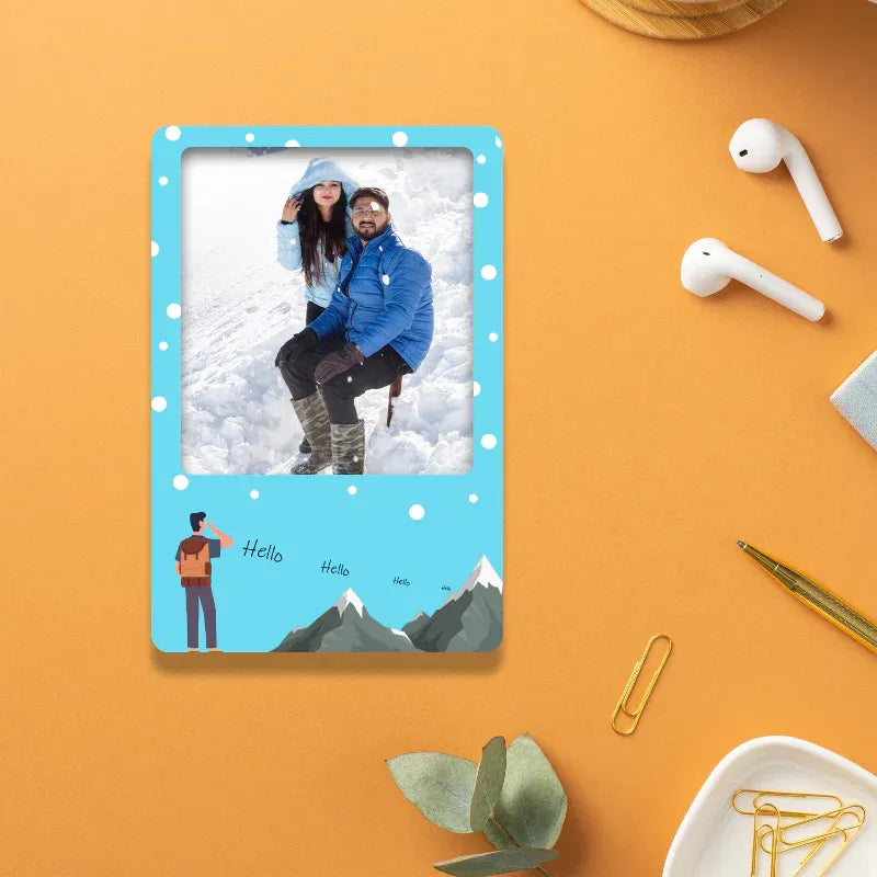 Phone case with a snowy photo of two people on a blue background, placed on an orange surface with accessories.
