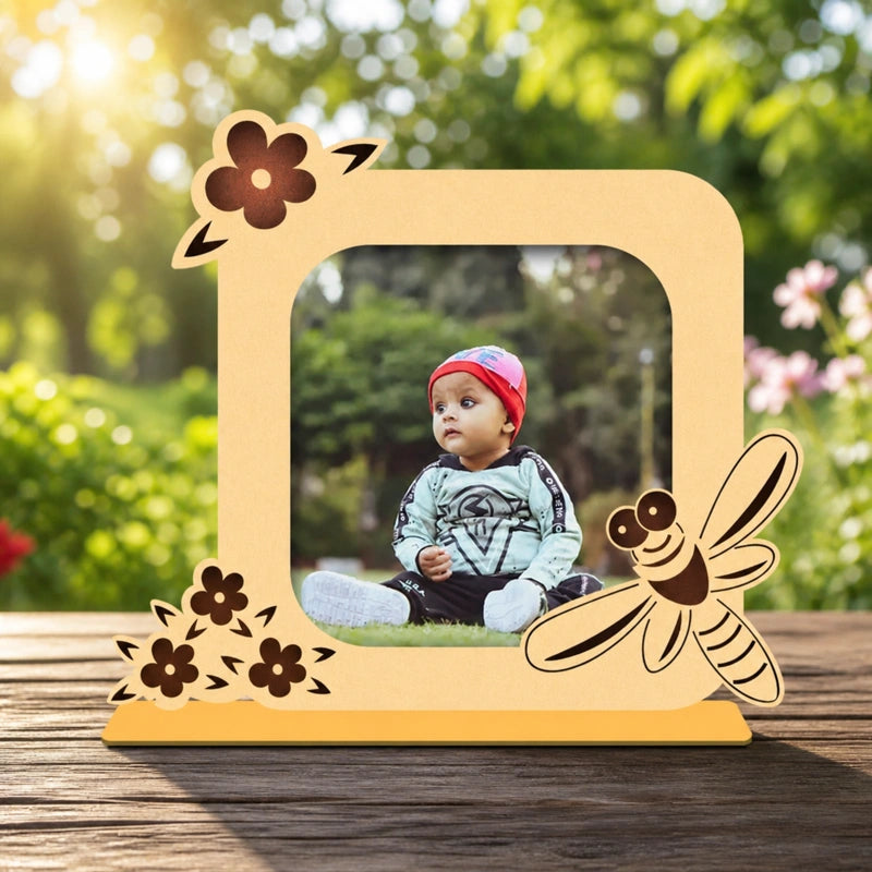 Wooden photo frame with floral and bee designs on a wooden surface with a blurred natural background