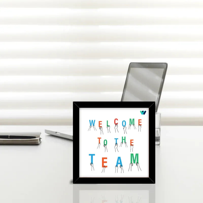 Framed artwork with 'Welcome to the Team' text on a desk with office supplies.