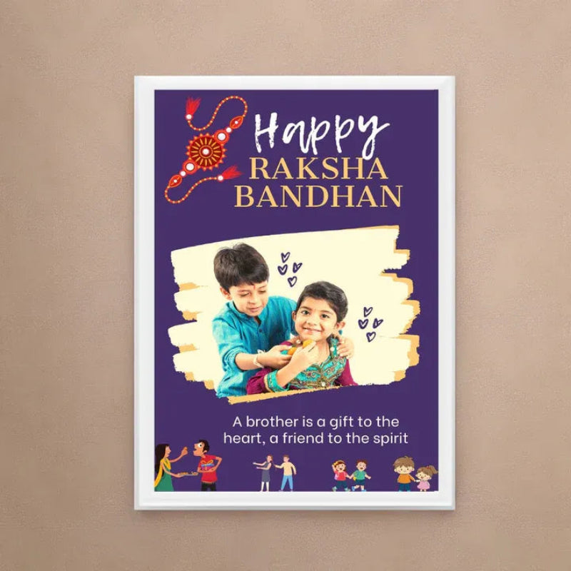 A framed vertical poster celebrating Raksha Bandhan, featuring a purple background, a decorative red and gold rangoli motif, a photo of a brother and sister, and the text 'Happy Raksha Bandhan' and 'A brother is a gift to the heart, a friend to the spirit.' The poster is displayed against a plain beige wall.