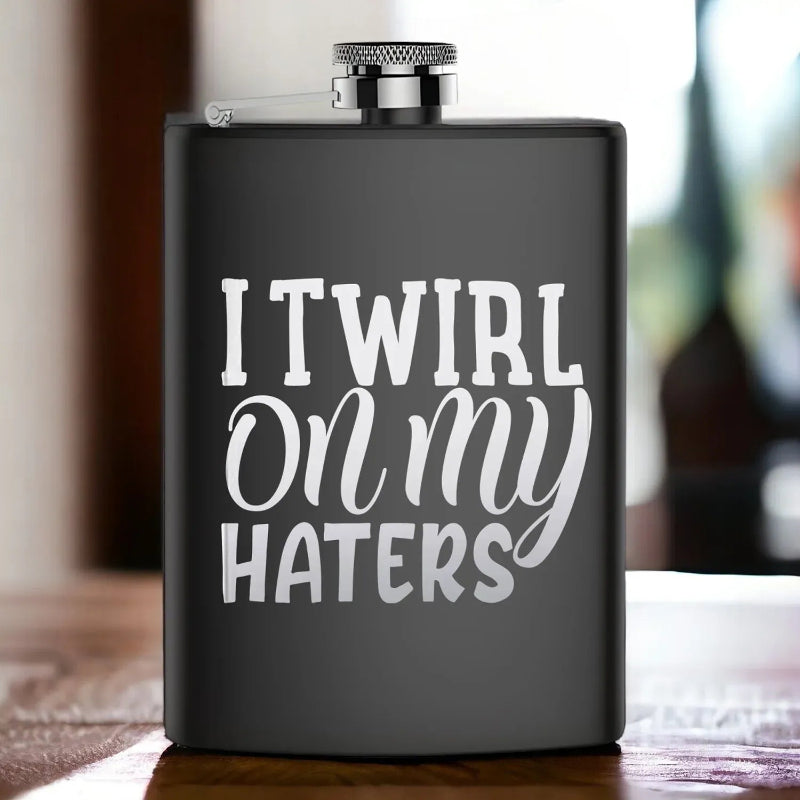 Black flask with 'I Twirl on my Haters' text on a wooden surface.
