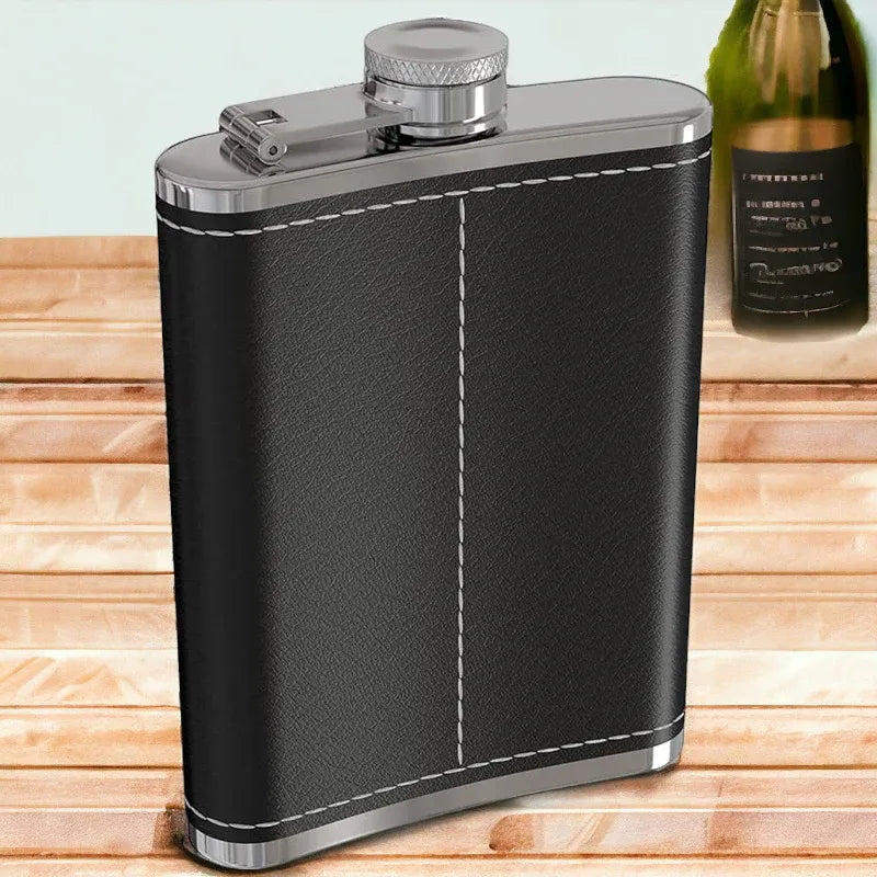 Black leather flask with silver accents on a wooden surface, next to a bottle of champagne.