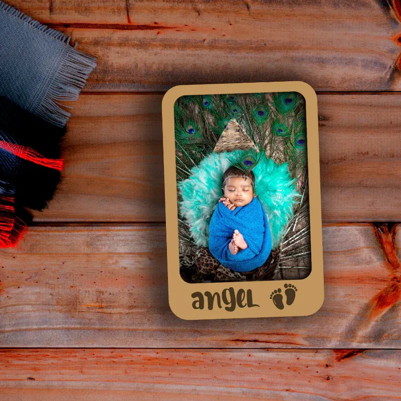 Baby in a blue outfit surrounded by peacock feathers in a decorative frame on a wooden surface.